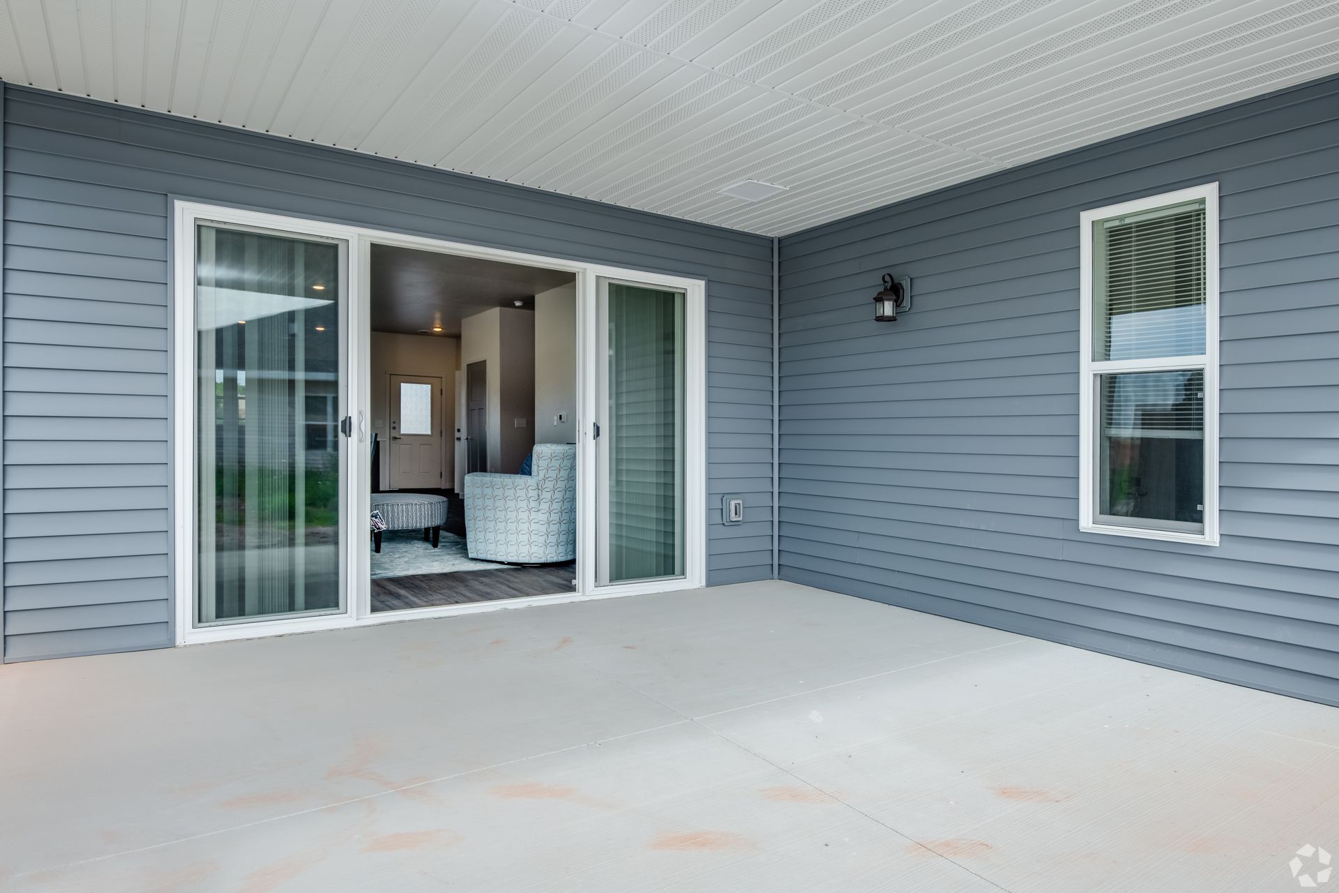 Covered patio with gray siding, large sliding glass doors, and a small window