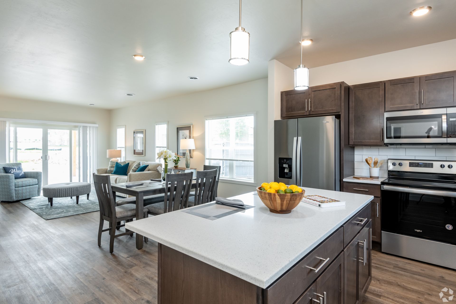 Open-concept kitchen and dining area with island, stainless appliances, and gray furniture