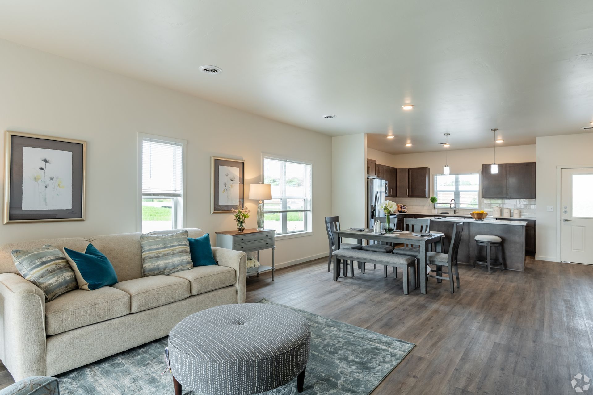 Open-concept living room and kitchen with beige sofa, gray ottoman, dining table, and wood floors