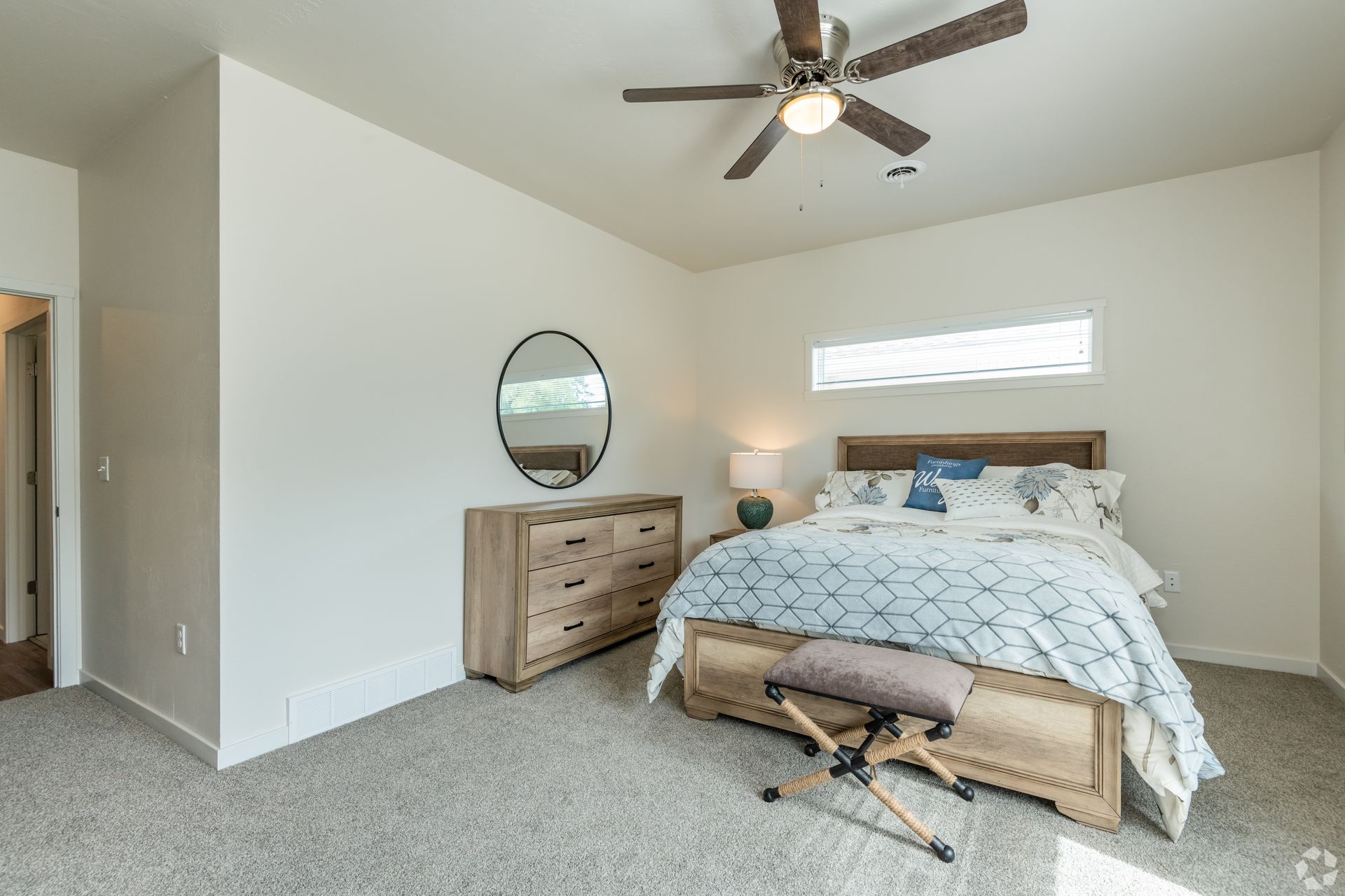Bedroom with a wicker bed, dresser, round mirror, ceiling fan, and small window light.