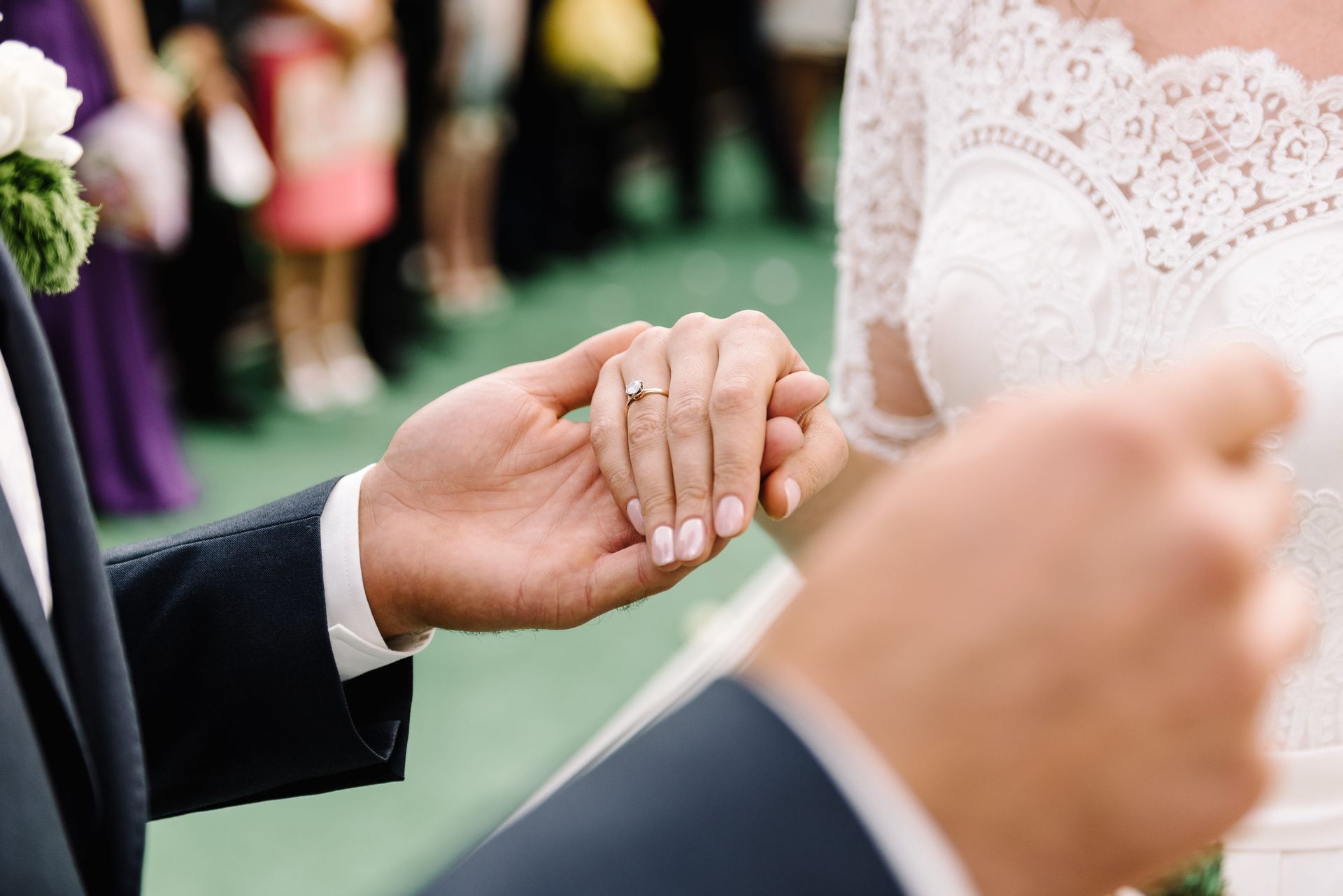 Close-up of two people holding hands during a wedding ceremony, with lace dress and suit visible