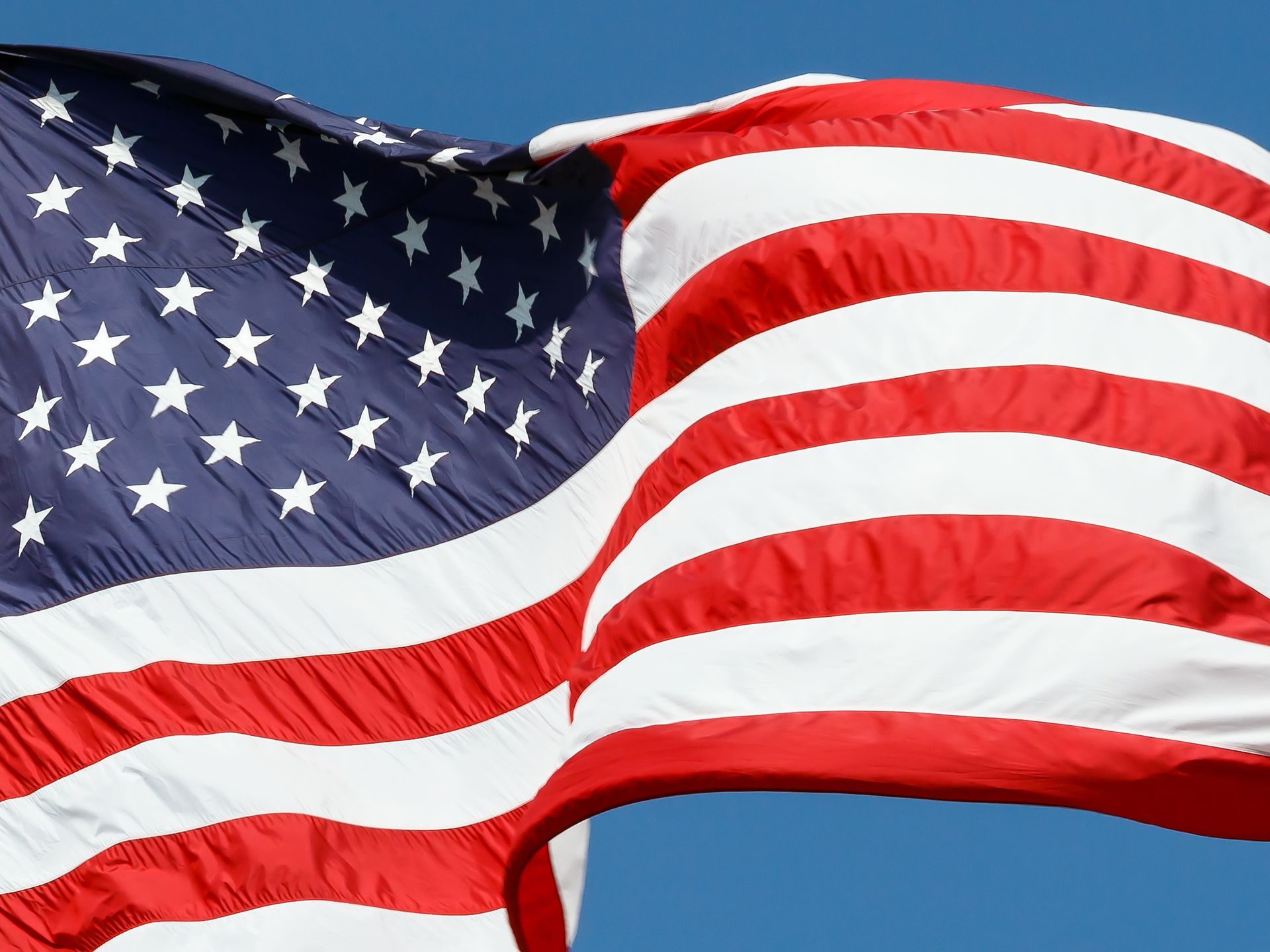 American flag waving in the wind with red and white stripes and a field of white stars on blue.