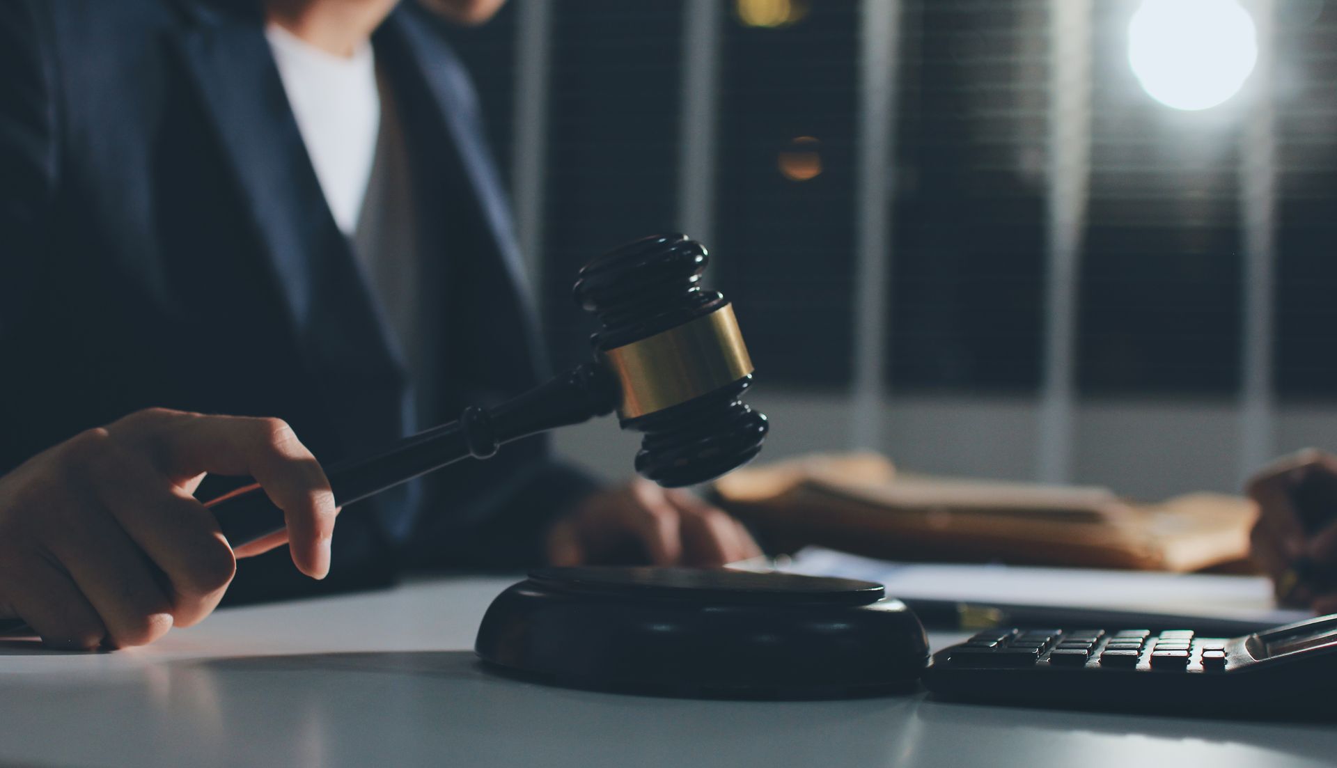 Person in suit holding a gavel, ready to strike on a wooden block, indoors.