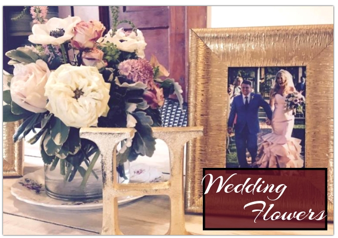 Wedding flower arrangement with white roses in a vase beside a framed wedding photo and “Wedding Flowers” sign