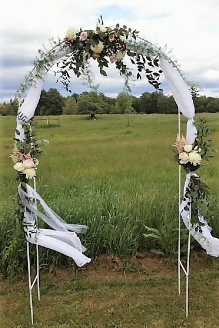 Floral wedding arch with white draping in a grassy field under a cloudy sky