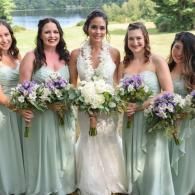 Bride with bridesmaids holding bouquets in mint-green dresses outdoors by a lake