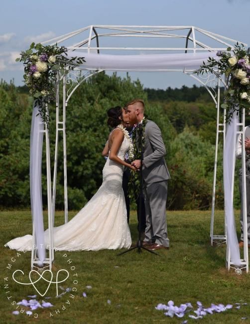 Bride and groom kissing under a white floral wedding arch outdoors