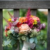 Bright mixed bouquet with peach, pink, and purple flowers on a wooden fence backdrop