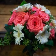 Pink roses and white daisies arranged in a bouquet with green leaves on a wooden surface