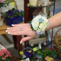Hand wearing a white and blue flower wrist corsage over a flower shop display