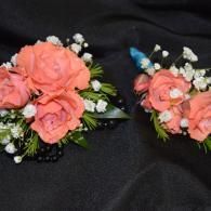 Coral rose floral corsages with baby’s breath and greenery on a black fabric background