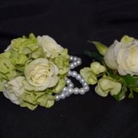 Two white and pale green floral corsages with pearl accents on a black background