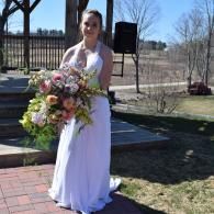 Woman in a white dress holding a bouquet outdoors on a brick path, with a speaker and fence in the background
