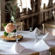 White-clothed restaurant table with folded napkins, upside-down glasses, and a floral centerpiece on a wooden base
