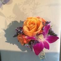 Orange rose and purple orchid corsage with glittery stem, lit against a wall shadow