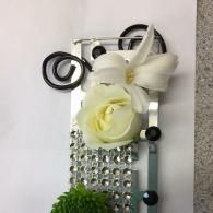 Decorative silver and white floral embellishment with gems and ribbons on a textured panel