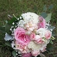 Pink and white rose bouquet with greenery, held outdoors against grass.