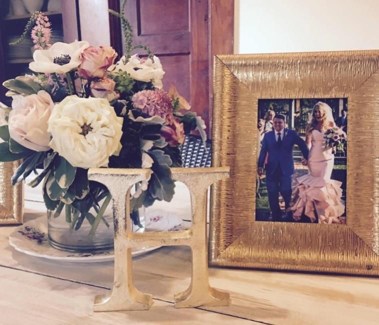 Framed wedding photo beside a white floral bouquet and gold candle holder on a table
