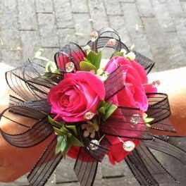 Pink rose corsage with black ribbon and small white accents, held in a hand outdoors