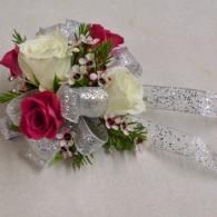 Pink and white rose corsage with silver ribbon and glittery bow on a light background
