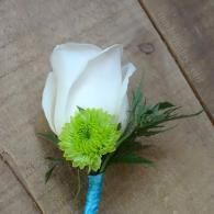 White rose boutonniere with a bright green flower on a blue-wrapped stem on wood floor