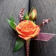 Orange rose boutonniere with purple ribbon and green leaves on gray fabric background