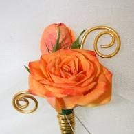 Orange rose boutonniere with gold spiral accents and a small bud on a white background