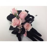 Black gloves holding a pink floral corsage with roses and small white blossoms
