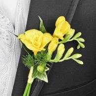 Yellow boutonniere with roses and green accents pinned to a black suit lapel