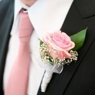 Pink rose boutonniere on a black suit with a pink tie