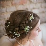 Braided updo with small white flowers against a blurred brick wall