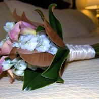 White and pink bridal bouquet with green leaves and satin ribbon on a bed