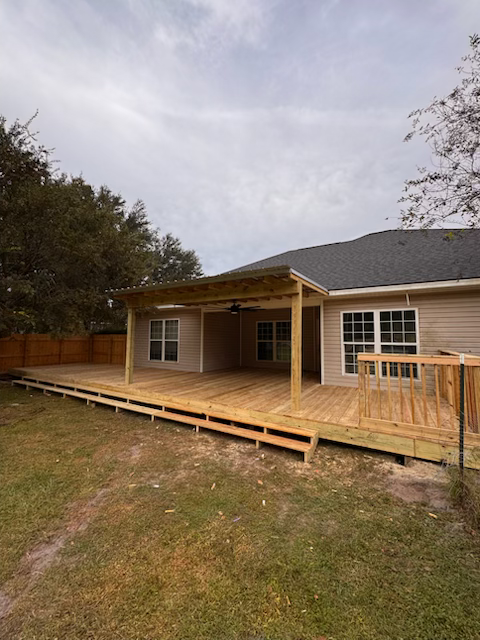 Covered wooden porch with railing beside a gray house, overlooking a grassy yard.