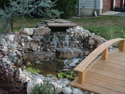 A wooden bridge over a pond with a waterfall in the background