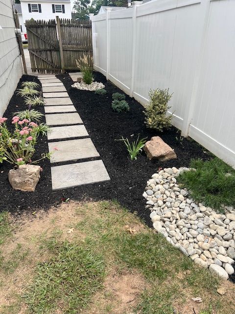 A walkway leading to a white fence in a backyard.