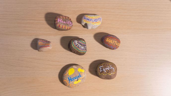 Seven painted rocks with words on a light wood surface.