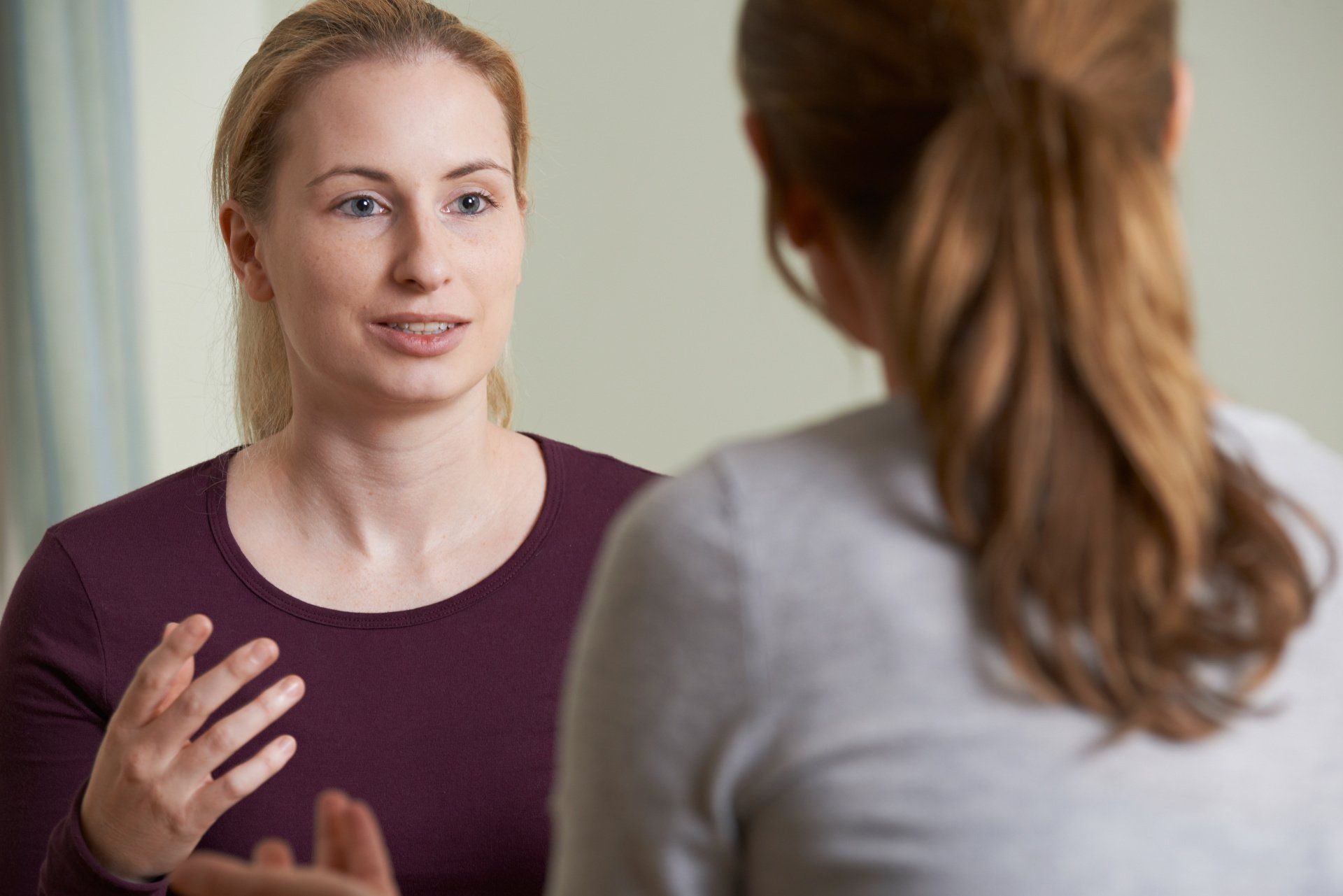 Woman in maroon top talking to another woman; indoors.