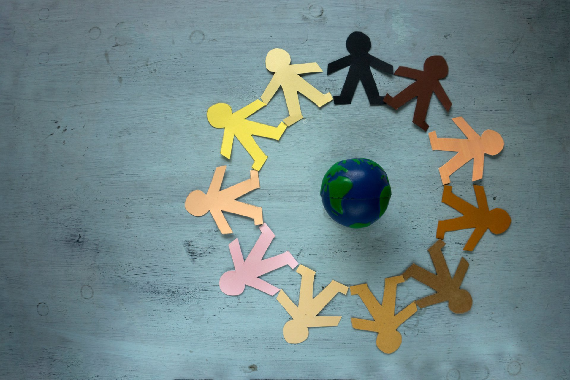People of diverse skin tones holding hands around a globe, representing global unity.