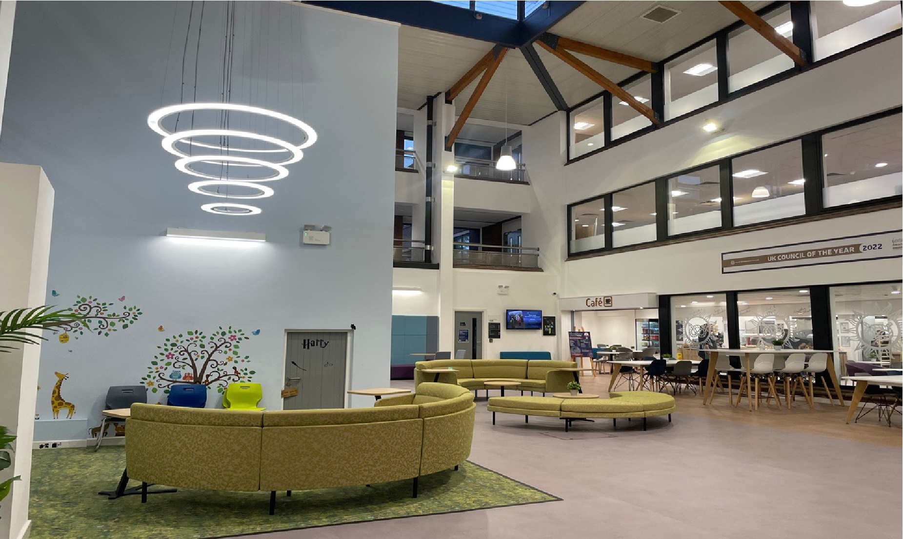 Modern school reception area with curved green sofa, large windows, and a circular light fixture.