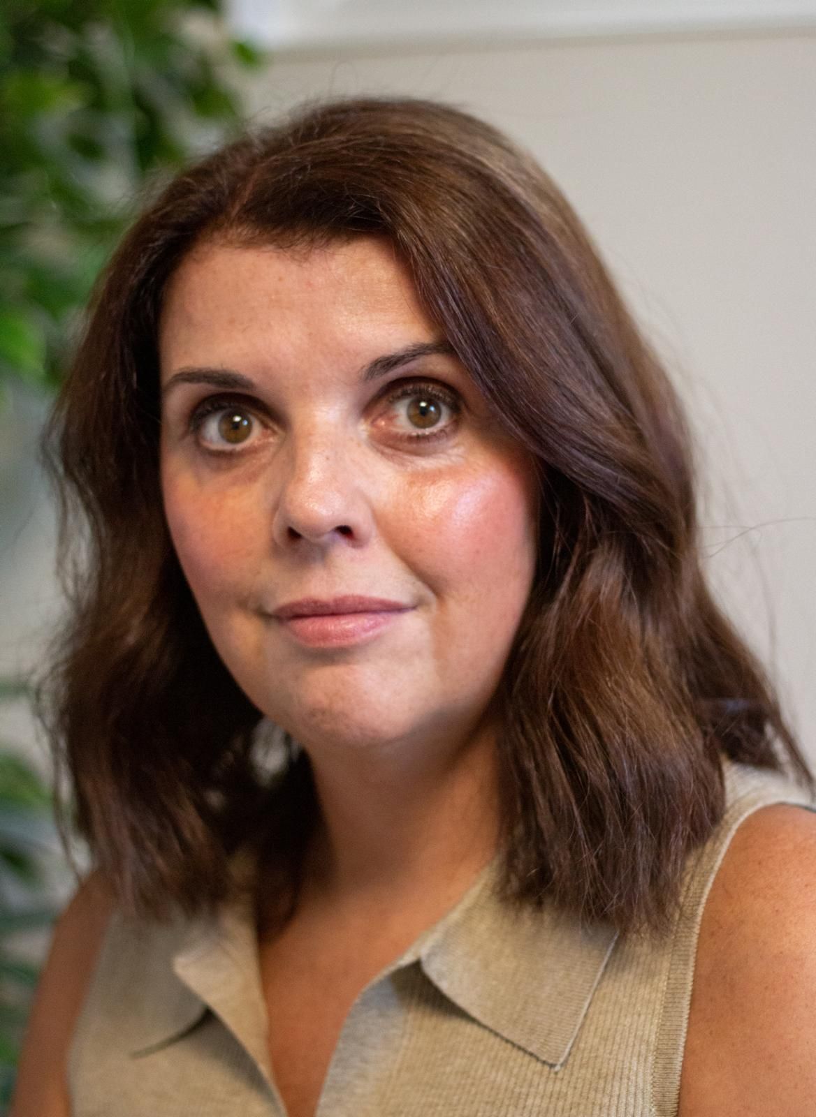 Woman with brown hair, light skin, wearing a beige top, looking forward.