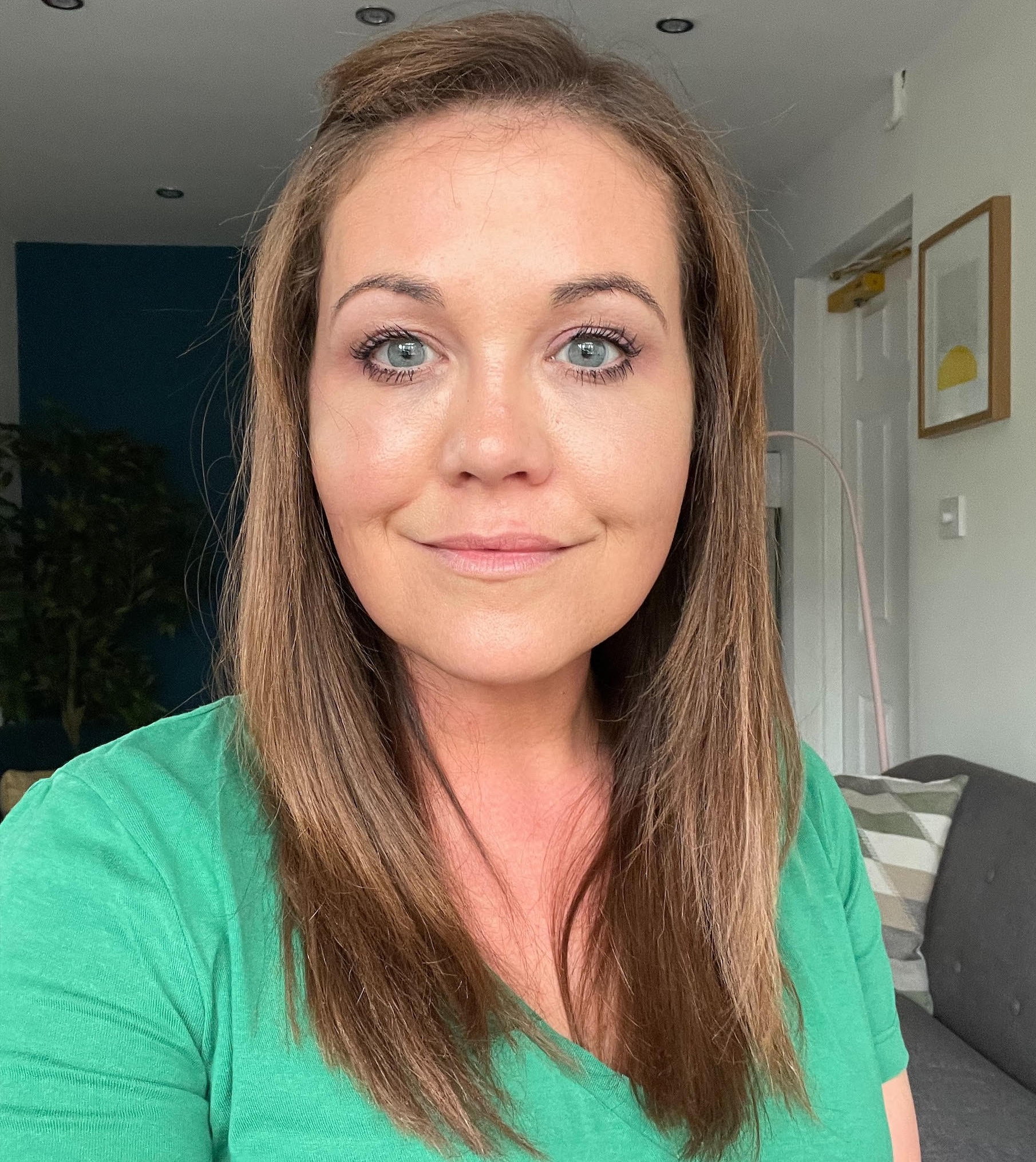 Woman with brown hair in a green shirt smiles at the camera, inside a home.