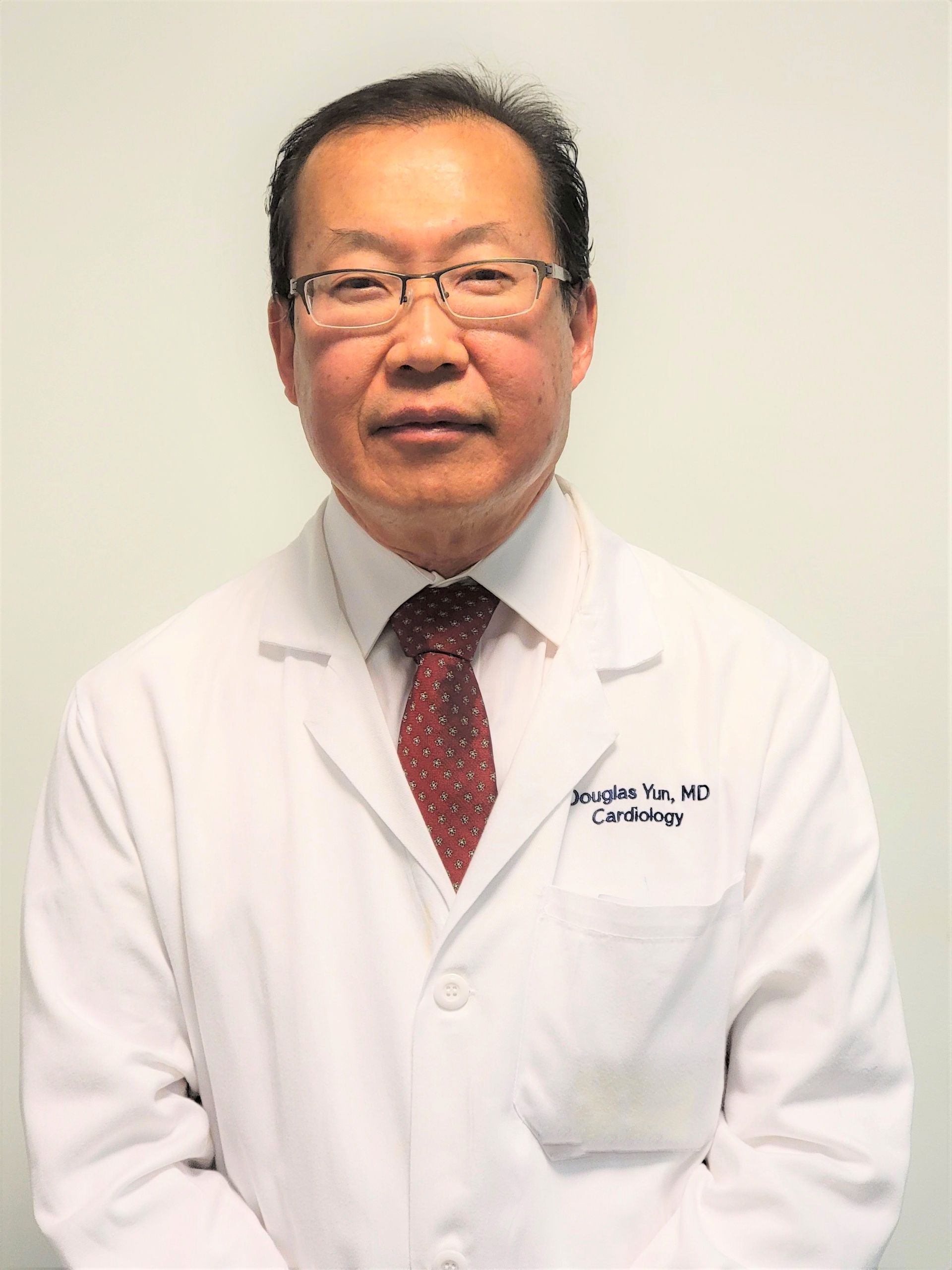 Doctor in a white lab coat and red tie standing against a plain wall.
