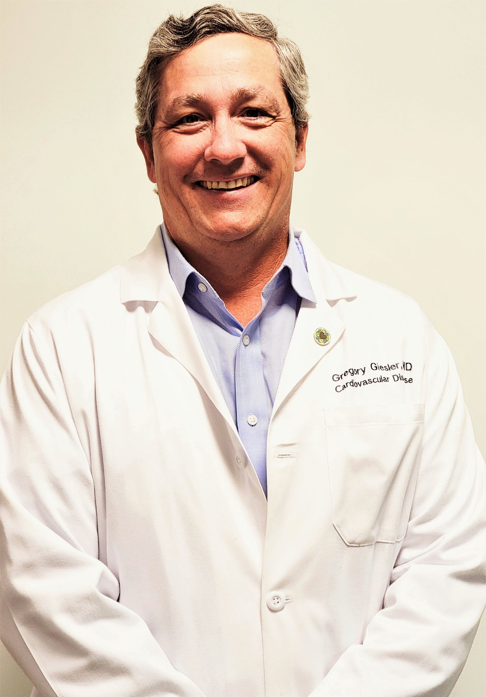 Smiling doctor in a white lab coat standing against a plain light background.