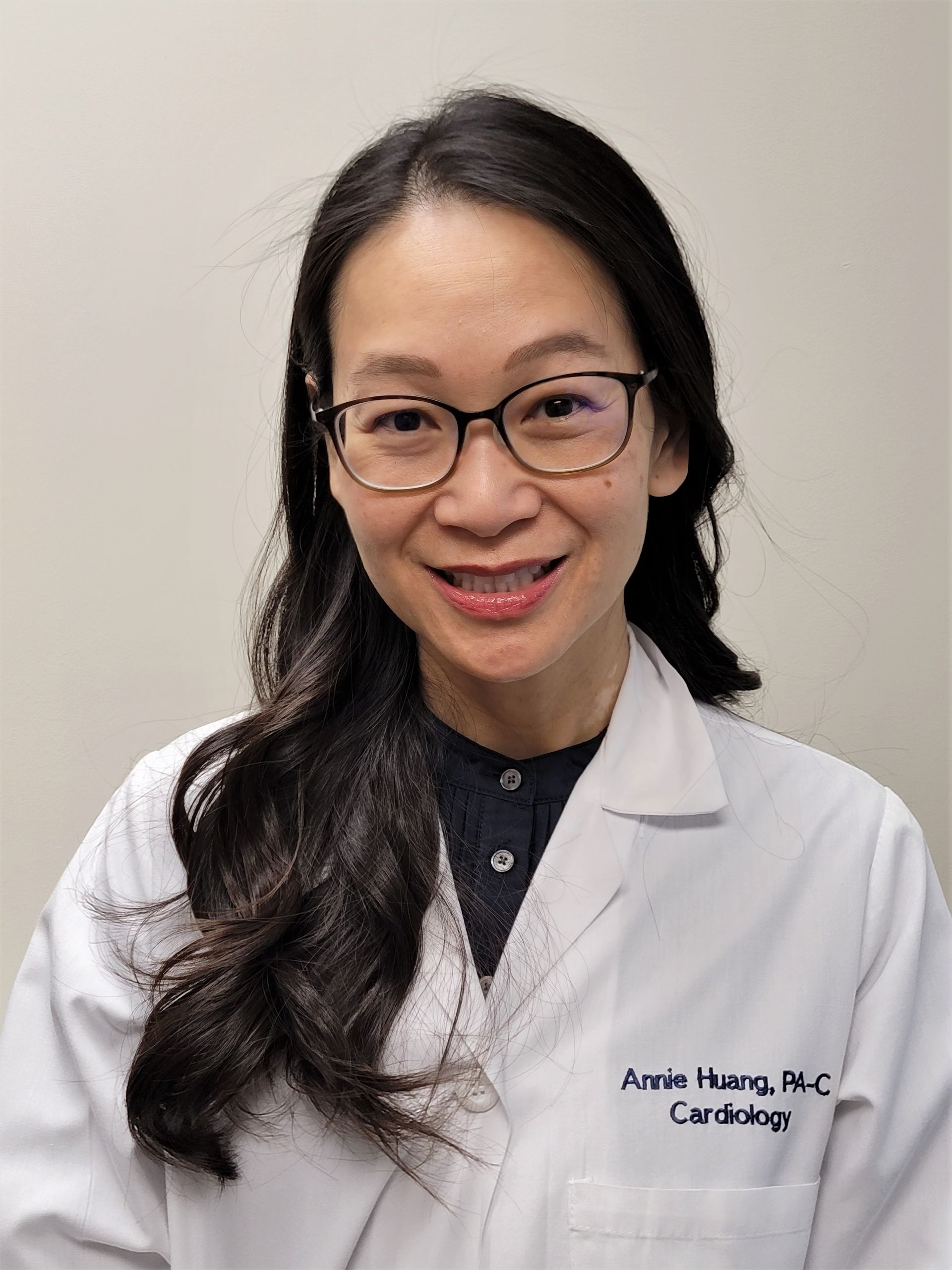 Smiling medical professional in glasses and white coat against a plain background