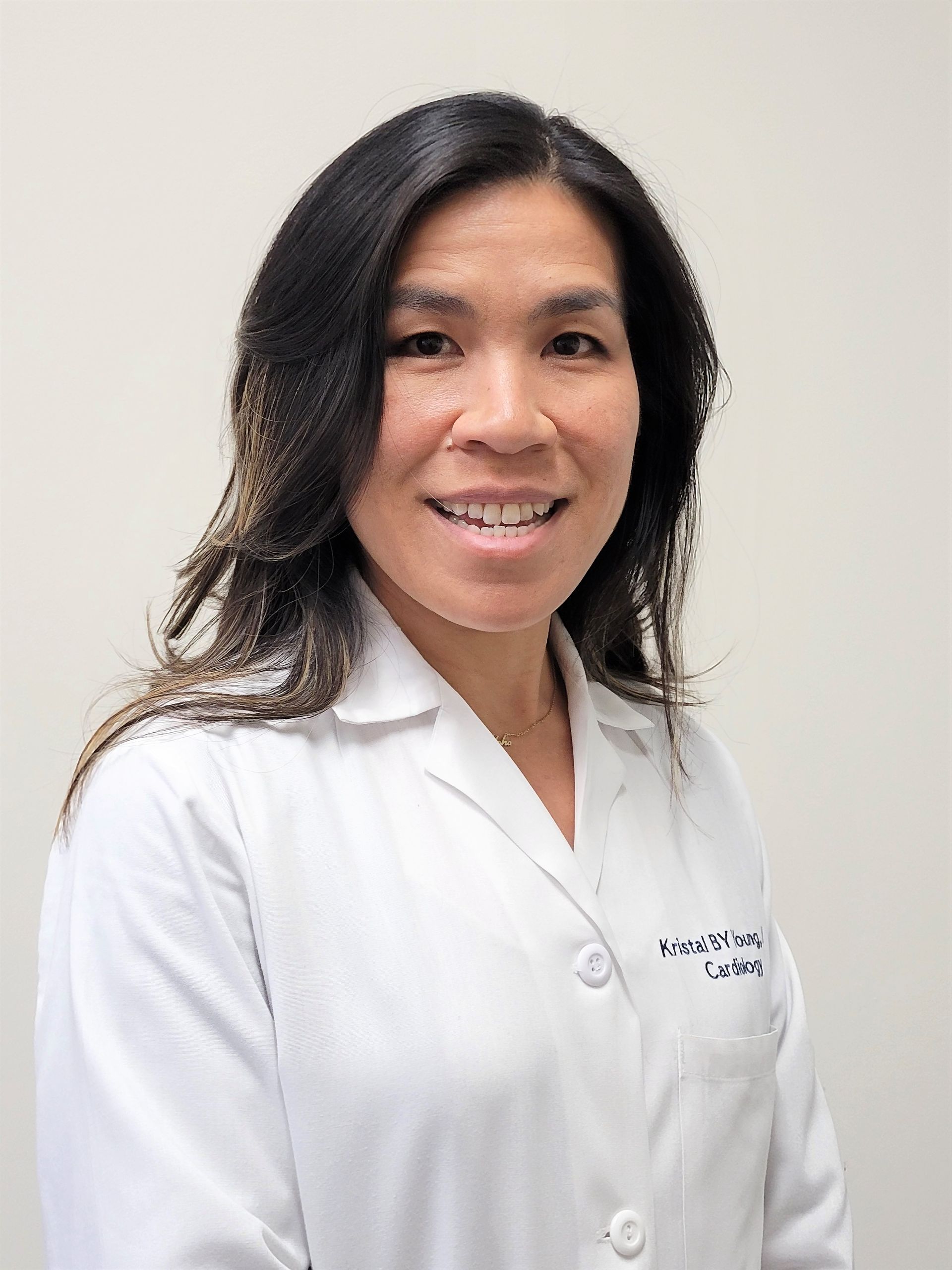 Smiling clinician in a white lab coat standing against a light wall.