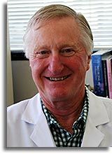 Smiling doctor in a white coat standing indoors with bookshelves in the background