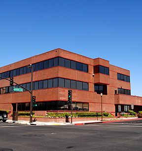 Red-brick office building with dark windows on a street corner under a clear blue sky