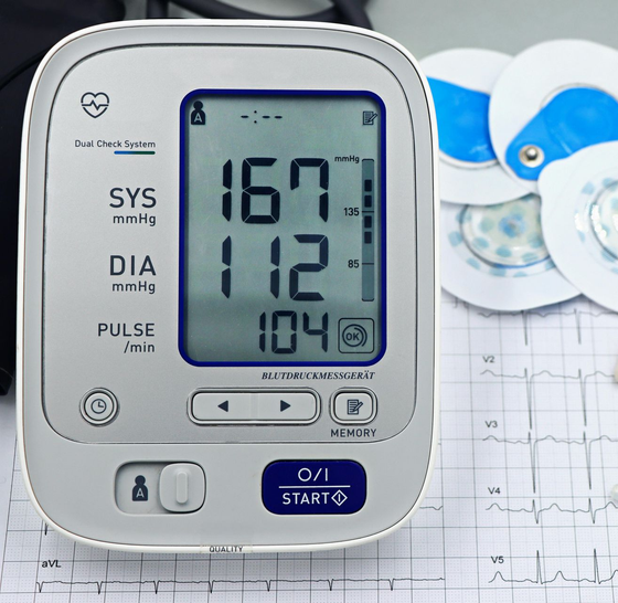 Blood pressure monitor showing 167/112 with pulse 104, beside a stethoscope and chart.