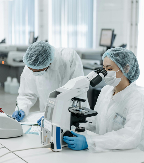 Scientists in lab coats using a microscope in a bright laboratory