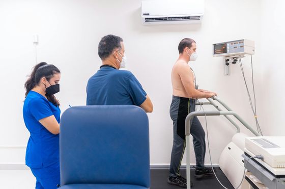 Three people in a clinic room, one using a treadmill while another monitors equipment.